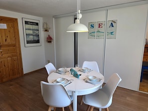 A dining area with a round table, white chairs, and a hanging light fixture. - Vacation apartment Alfredo (Wustrow)