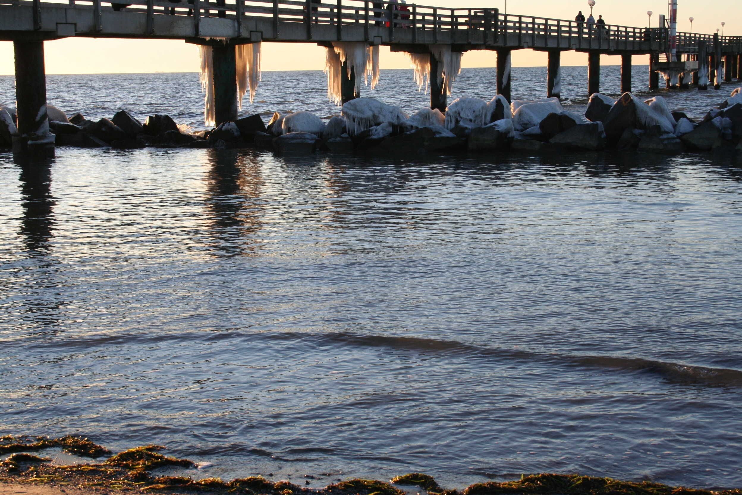 A pier extending into calm water with ice formations on rocks and a wooden walkway.