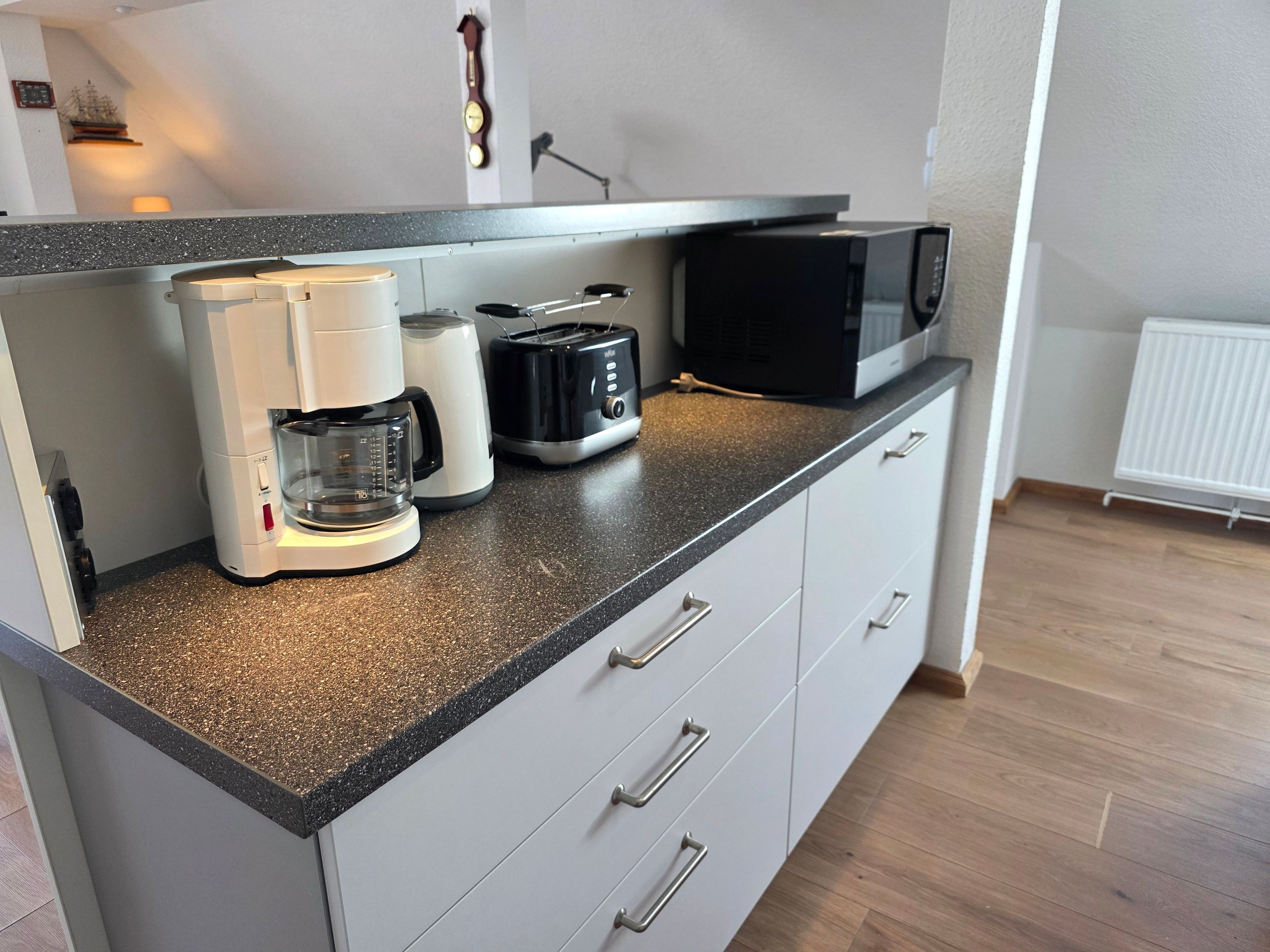 A kitchenette with a coffee maker, toaster, microwave, and a kettle on a speckled countertop.