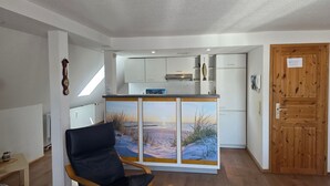 Una cocina moderna con armarios blancos, una puerta de madera y vistas a un paisaje nevado a través de un panel de vidrio.