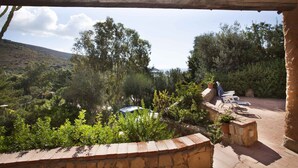 Eine Terrassenfläche mit Blick auf eine gebirgige Landschaft, umgeben von Grünpflanzen und einer Steinmauer.