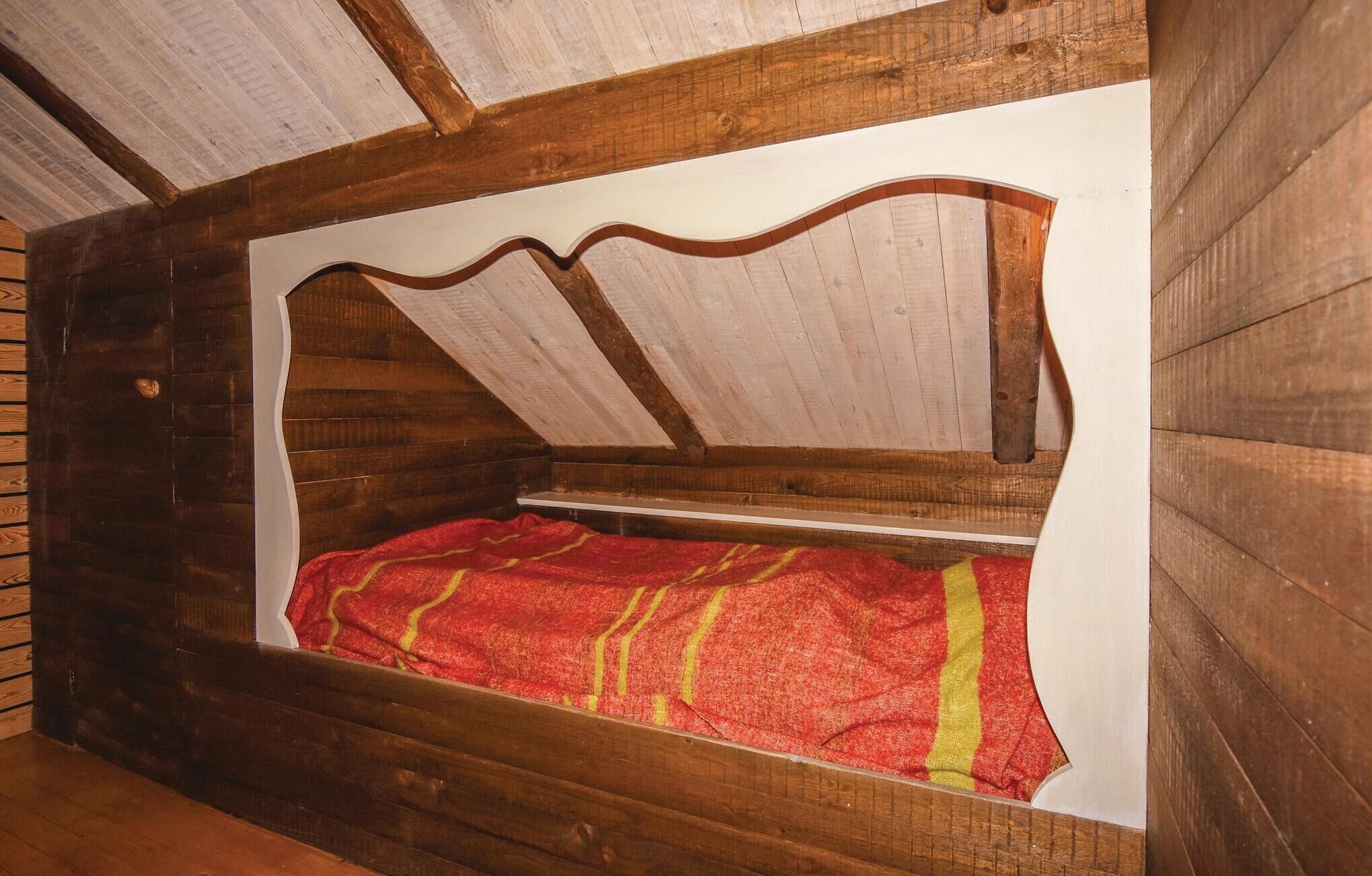 Una habitación tipo cabaña de madera con una cama, techo inclinado y paredes de madera.