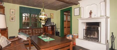 Een woonkamer met een open haard, een leren bank, een houten salontafel en een groen gestreept vloerkleed.