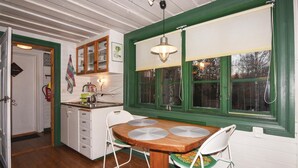 Una cucina con un tavolo di legno, sedie bianche, una finestra con persiane verdi e una lampada a sospensione.