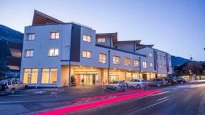A multi-story hotel with a modern design, featuring a prominent entrance, a parking area, and a view of the surrounding landscape. - Double room Hochzillertal 2 - Aparthotel **** AlpTirol (Kaltenbach)