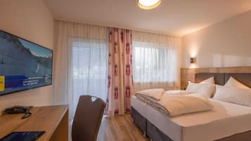 Ein Hotelzimmer mit Bett, Schreibtisch, Telefon, Tablet, Stuhl und einem großen Fenster mit Vorhängen.