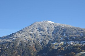 A mountain with a snow-capped peak, forested slopes, and scattered buildings at its base. - Double room Hochzillertal 2 - Aparthotel **** AlpTirol (Kaltenbach)