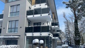 Un immeuble à plusieurs étages, doté de balcons, de grandes fenêtres et entouré d’un paysage enneigé.