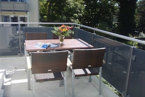 A balcony with a table, chairs, and a vase of flowers.