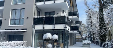 Un immeuble à plusieurs étages, doté de balcons, de grandes fenêtres et entouré d’un paysage enneigé.