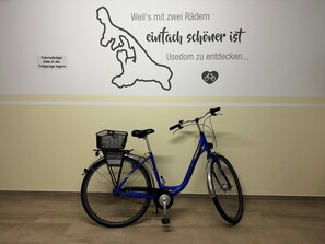 Ein blaues Fahrrad mit Korb und eine Wand mit einem deutschen Zitat sowie ein Schild mit der Aufschrift 'Fahradträger bitte in der Tiefgarage laden'.