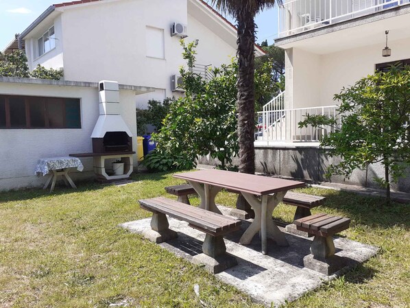 A patio with a barbecue grill, a table with benches, and a small table with a cloth.