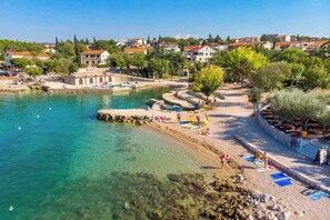 A coastal town with clear waters, a sandy beach, and buildings in the background.