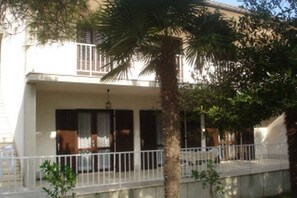 Een gebouw met twee verdiepingen, een balkon, witte leuningen en een palmboom op de voorgrond.