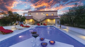 Ein Swimmingpool mit Liegestühlen und Kerzen, umgeben von Bäumen und einem Gebäude mit einer Treppe.