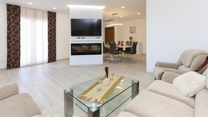 Ein modernes Wohnzimmer mit einem Glastisch, beigefarbenen Sofas, einem Flachbildfernseher und einem Kamin.