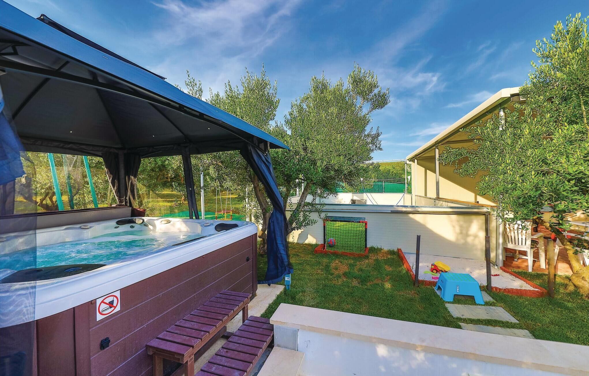 A hot tub with a covered roof, a small play area with a slide, and a fenced yard with trees.