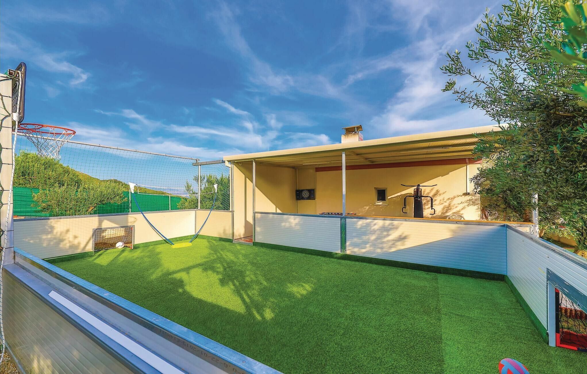 A pool with a netted area for water sports, a covered seating area, and a view of trees and hills.