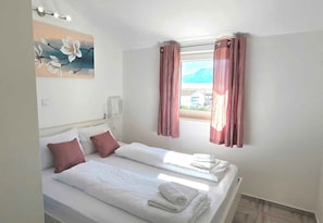 Habitación de hotel con dos camas, un cuadro en la pared, una ventana con cortinas y una mesita de noche con toallas.