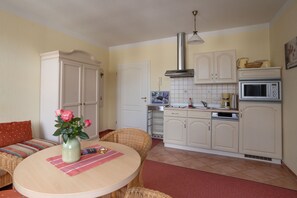 A kitchen with white cabinets, a microwave, and a sink. There is a dining table with a vase of flowers.
