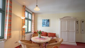 A room with a round table, wicker chairs, a white cabinet, and a window with curtains.