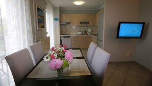 A dining area with a table set for four, a vase of flowers, and a kitchen in the background. - Holiday apartment with balcony and sea view (Šilo)