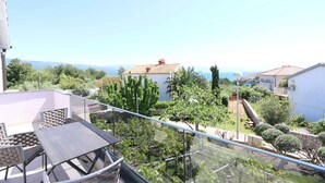 A balcony with a table and chairs, a view of a house with a tiled roof, and surrounding greenery. - Holiday apartment with balcony and sea view (Šilo)