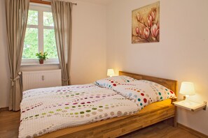 A bedroom with a wooden bed, a window with curtains, a radiator, a wall-mounted lamp, and a painting.