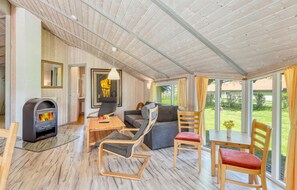 Un salon chaleureux avec une cheminée, des sièges confortables et de grandes fenêtres donnant sur l’extérieur.