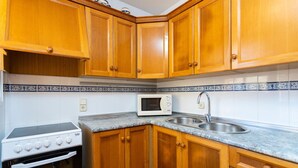A kitchen with wooden cabinets, a microwave, a sink, and a stove. - Cala Morlanda Palma d Mallorca (Cala Morlanda)