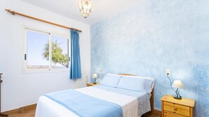 A bedroom with a bed, nightstands, a window with curtains, a radiator, and a view of trees. - Cala Morlanda Palma d Mallorca (Cala Morlanda)