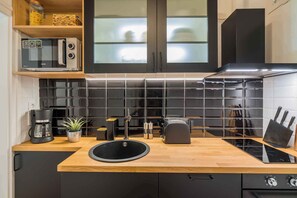 A modern kitchen with a black and white tiled backsplash, a wooden countertop, a built-in microwave, a coffee maker, a sink, and a stove. - Holiday apartment only 250 m from the sandy beach of the Golden Shore (Siófok)