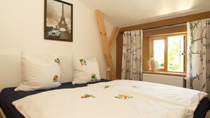 A bedroom with a bed, pillows with colorful designs, a window with curtains, and a framed picture of the Eiffel Tower on the wall. - Pfarrweg 10 PF-10 - PF-10 (Kühlungsborn)