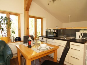 A cozy kitchen with wooden cabinets, a dining table set for two, and a large window with a view of greenery. - Pfarrweg 10 PF-10 - PF-10 (Kühlungsborn)