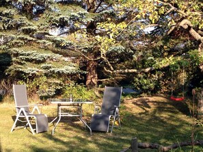 A garden with a table and two chairs, surrounded by trees and greenery. - Pfarrweg 10 PF-10 - PF-10 (Kühlungsborn)