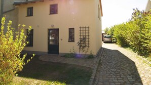 A two-story building with a stone-paved courtyard, a black door, and a small garden area with plants. - Pfarrweg 10 PF-10 - PF-10 (Kühlungsborn)
