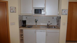 A compact kitchen with white cabinets, a microwave, a coffee maker, and a sink. - (225/1) 2-room apartment-Strandstrasse - apartment house Strandburg (Kühlungsborn)