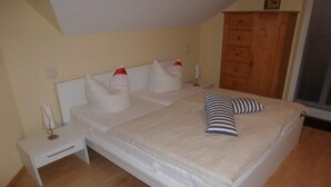 A bedroom with a bed, nightstands, a wooden wardrobe, and a window. - (225/1) 2-room apartment-Strandstrasse - apartment house Strandburg (Kühlungsborn)