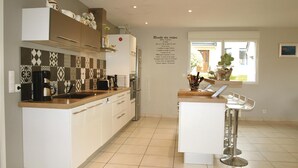 Una cocina moderna con armarios blancos, un salpicadero decorado y una cafetera. Se ve una ventana con vistas al exterior y un panel de recetas en la pared.