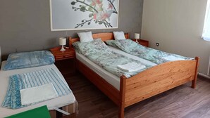 Quarto com cama de madeira, duas mesas de cabeceira, um criado-mudo, uma grande obra de arte floral na parede e uma janela com cortinas.