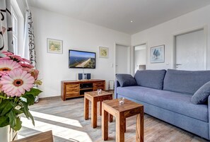 Uma sala de estar com um sofá cinzento, mesa de centro de madeira e uma televisão na parede.