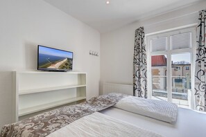Un dormitorio con una cama, un televisor en un estante, una ventana con cortinas y un radiador.