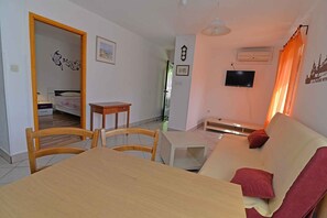 Een woonkamer met een bank, een aan de muur bevestigde televisie en een eettafel met stoelen.