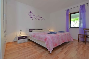 Een slaapkamer met een bed, nachtkastje, lamp en raam met gordijnen.