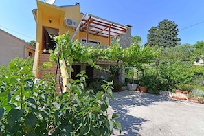 Een geel gebouw met een gevel van natuursteen, een houten pergola en potplanten.