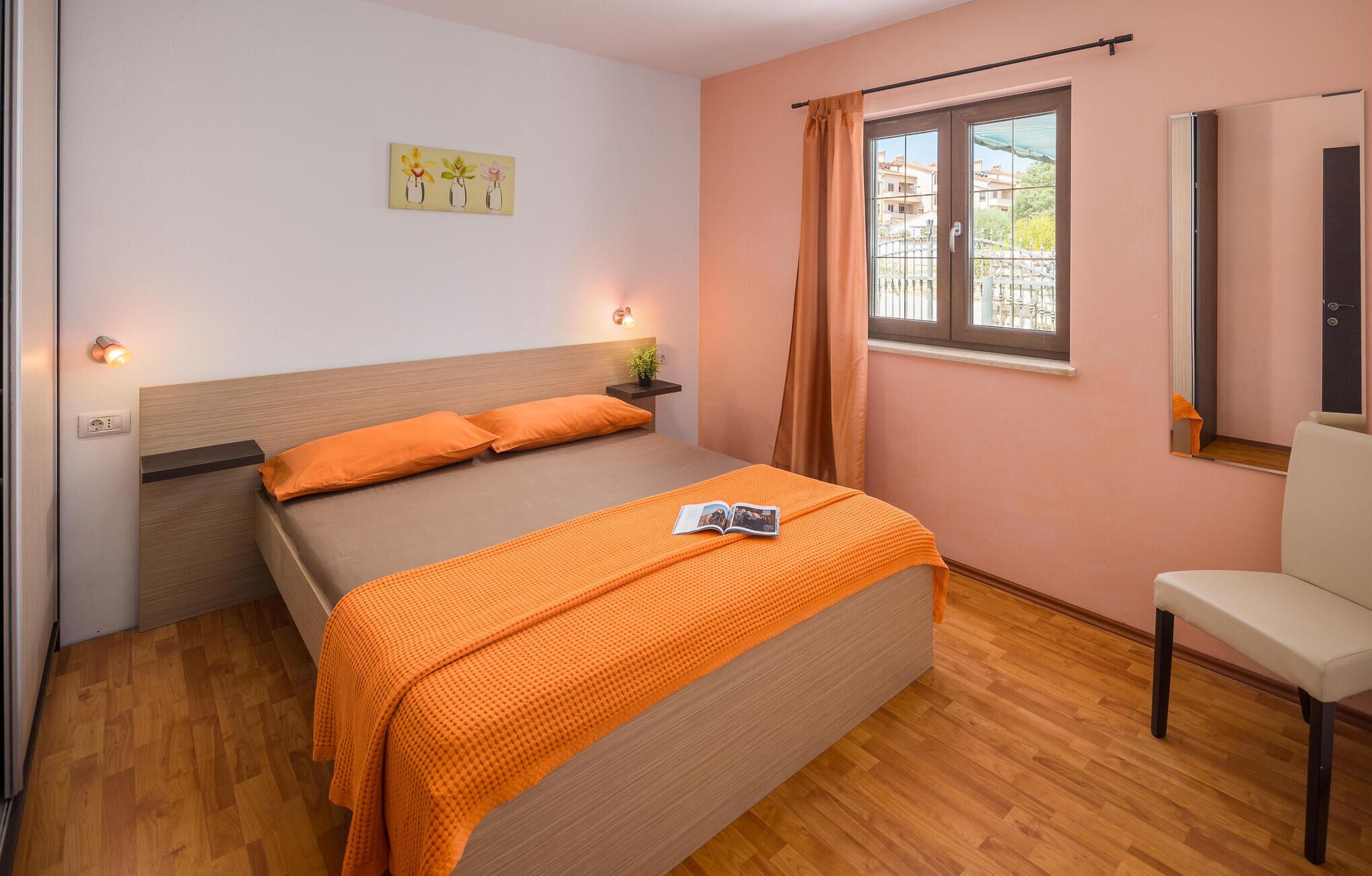 Une chambre à coucher comprenant un lit, une table de chevet, une chaise, une fenêtre avec des rideaux et une étagère murale agrémentée d’une plante.