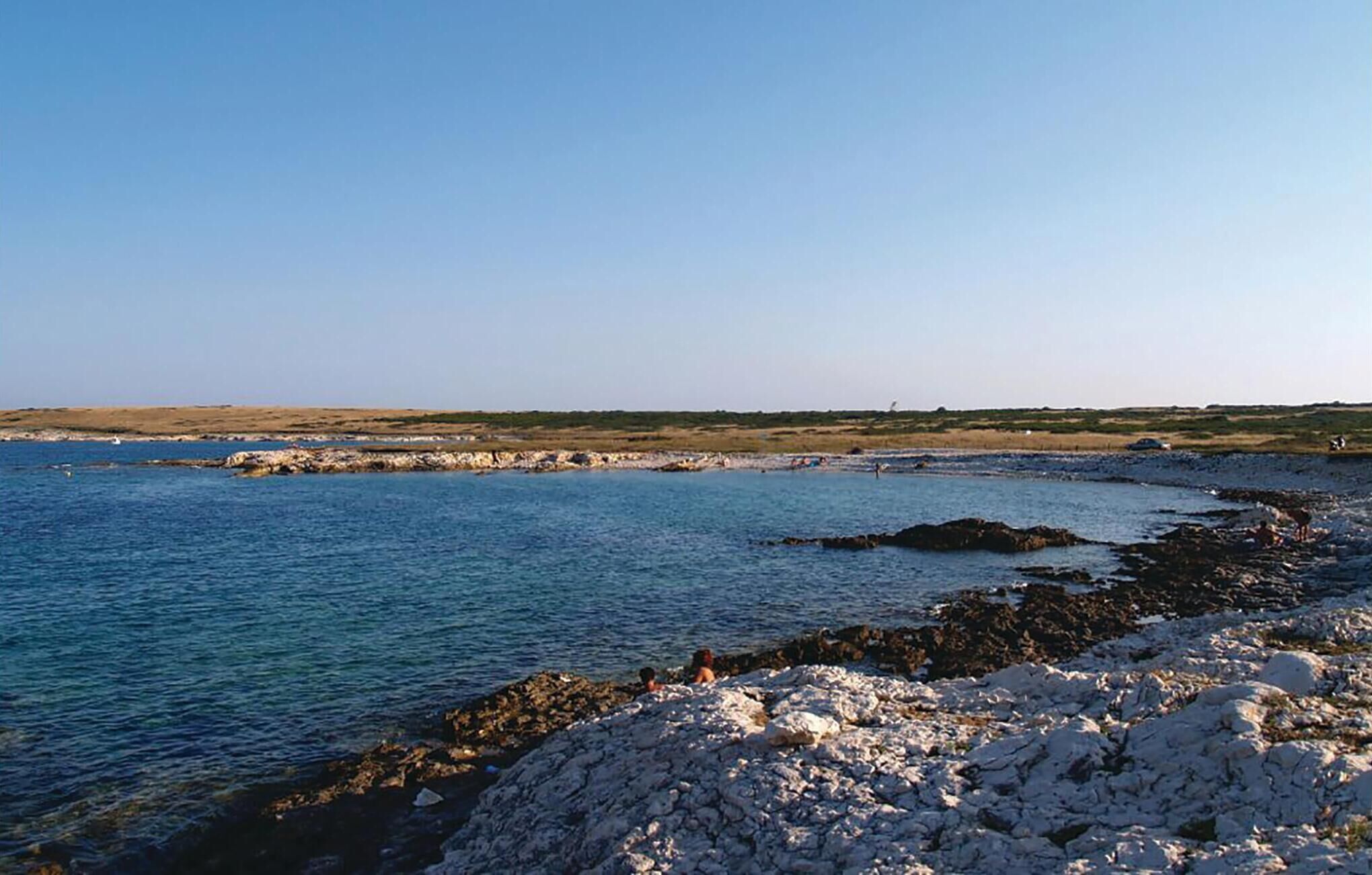 Paesaggio costiero con scogliere rocciose e mare calmo.