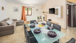 En moderne stue med spiseområde, sofa, fjernsyn og et vindue med gardiner.