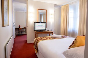 Una habitación de hotel con una cama, un escritorio con una computadora, una silla y un espejo.