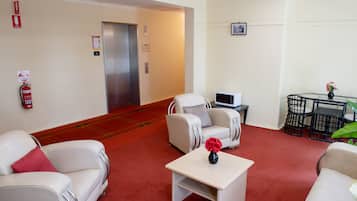 Eine Hotelhalle mit rotem Teppich, weißen Sofas, einem kleinen Tisch mit einer Vase, einer Mikrowelle und einem Feuerlöscher.